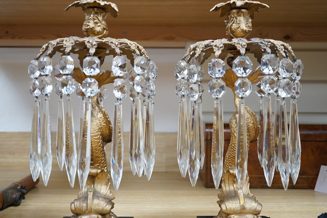 A pair of William IV gilt metal candlesticks, the stems formed as dolphins, with glass lustre drops, raised on square slate bases, 37cm high